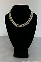 Full front view of vintage silver-tone leaf design necklace on black bust stand.