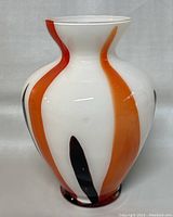 White Murano glass vase with orange and black vertical swirl pattern, rounded shape with flared rim.