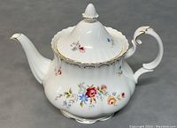 Front side view of the teapot showing floral pattern, gold-rimmed lid, curved spout and ornate handle.