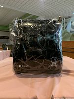 Front view of one wrapped black/smoke grey Kruger Mini Titan paper towel dispenser showing brand logo and some packaging reflection.