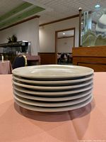 Stacked view of approximately 8 off-white circular plates showing thickness and condition of edges.