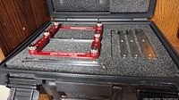 Open foam-lined case showing red anodized gauge frame at left and three steel blades plus hex key at right