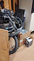 Overall view of stainless steel canister vacuum with hoses in wire basket and boxed pump next to Delta unit