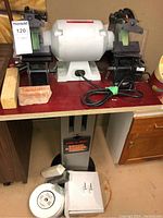 Front view of bench grinder mounted on stand showing green wheels and red tabletop