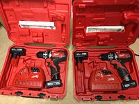 Two open red Milwaukee carrying cases each containing a cordless drill, charger, and battery