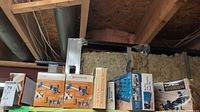 Photo showing packed boxes of Rockler Pipe Clamp Bench Blocks, Brass Router Bushing Set, Rockler Countersink Bit Set, and Template Guide Kits arranged on a wooden ledge with wall insulation behind.