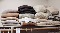 Two stacks of neutral and cream sweaters on a closet shelf