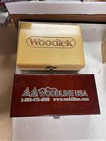Two wooden cases closed: natural-finish WoodTek box on top, red-stained Woodline USA box below.
