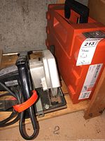 Circular saw and red tool carrying case side by side on wooden shelf