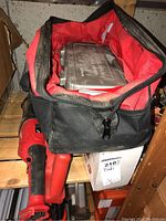 Soft tool bag open on shelf showing red lining and plastic case of bits