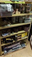 Metal shelving unit with jars of screws, boxes of sanding discs, table saw pushers and clamps