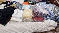 Overall view of multiple folded men's shirts on a bed, various colors and patterns in clear plastic packaging