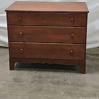 Front view of vintage dark brown wooden 3 drawer chest showing closed drawers and round wooden knobs.