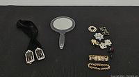 All items laid out showing the mirror, pins, bracelets, and belt on a dark background.