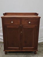 Front view of the antique wooden cabinet showing two drawers with white knobs and two doors beneath.