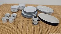 Full set of blue and white ceramic dishes including casserole dishes, jam/jelly jar, plates, bowls, and ramekins arranged on woven mat