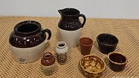 Overview of entire lot showing all nine ceramic stoneware items including the bean pot, milk pitcher, various jars and four small dishes.