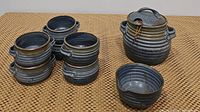 Photo showing six blue ceramic double-handled bowls stacked in two stacks of three, with one bowl and the soup tureen visible on a wicker mat surface.