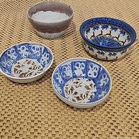 Four bowls displayed on woven mat: pottery drip glaze bowl, Christmas ceramic bowl with reindeer, and two blue and brown porcelain bowls.