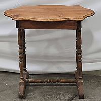 Side view of table showing the curved and scrolled top, turned legs, and stretcher base