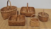 Photo of five woven baskets of various shapes and sizes arranged on woven mat, showcasing size and handle details.