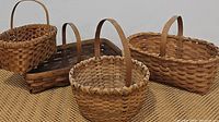 Set of four handled baskets of various shapes arranged on woven mat, showing their sizes and handle styles