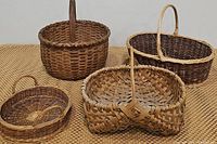 Four large woven baskets grouped on a woven mat surface showing variety of shapes and woven styles.