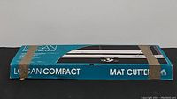 Box of Logan Compact Mat Cutter sealed with tape, showing compact size and brand name.