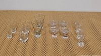 Front view of all glasses including shot glasses, urn-shaped, cocktail glasses and footed liquor glasses arranged on woven surface