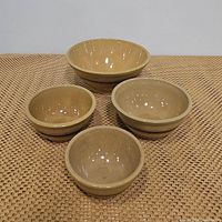 Four nested brown ceramic bowls with horizontal stripes stacked on a woven surface.
