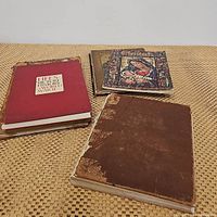 Four old books shown on woven textured cloth. Includes two Christmas themed books, a large worn brown leather-bound book, and a red hardcover history book.