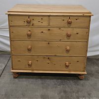 Front view of rustic antique pine chest of drawers, showing closed drawers with round wooden handles and natural wood grain.