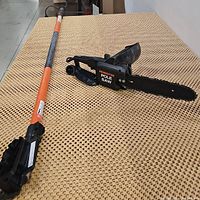 Full view of the Remington pole saw with orange extendable pole laid on a textured fabric surface, showing the cutting head and pole.