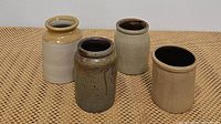 Four antique stoneware pottery pieces arranged on woven mat background showing various colors and finishes.