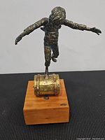 Front view of bronze sculpture showing boy balancing on barrel atop wooden base