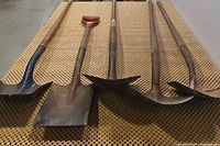 Photo of five used shovels laid out on a surface, showing different blade shapes and wooden handles