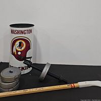 Photo showing Washington Redskins metal trash can, dumbbell barbell with weights, and hockey stick laid out on black mat