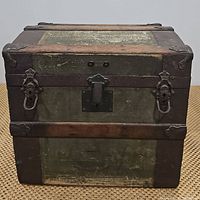 Front view of the closed antique wooden steamer trunk, showing metal hardware, locks, and wooden trim.