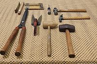 Photo showing four hammers with wooden handles, four vintage folding rulers, red gardening scissors, and hedge & grass shears laid out on a woven surface.
