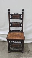 Front view of the antique wooden chair showing ornate high back with carved panels and wooden seat