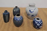 Set of five ceramic vases on woven surface, showing variety of shapes and blue tones
