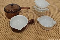Full view of Corning Ware amber glass saucepan with lid, white and brown handled soup bowl, and three vintage Pyrex sandalwood bakeware dishes with leaf and ivy patterns.