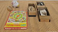 Overview photo showing seller's items including puzzle clock box, ceramic and glass piggy banks, and three shoe boxes with vintage kids shoes.