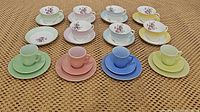 Overview of all tea cups and saucers including Colclough floral sets and Hazel Atlas pastel Little Hostess sets arranged on a mat surface.