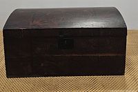 Photo of the closed chest showing its curved wooden top with a dark finish and front locking mechanism.