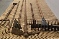 Photo showing side-by-side arrangement of hand thatching rake, pickaxe, garden hoe, and pitchforks to illustrate items included in the lot.
