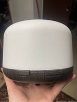 Front view showing buttons for light, timer, mist control and power on/off with dark wood grain base and white plastic top.