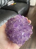 Amethyst crystal cluster held in hand showing multiple pointed purple crystals and texture.