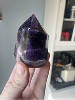 Handheld amethyst crystal tower showing deep purple color and polished facets from one angle.