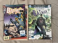 Two Batman comic books laid side by side. The left comic is Knightfall series with price tag and visible rip. The right comic is All-Star Batman issue 14 with a detailed dark cover.